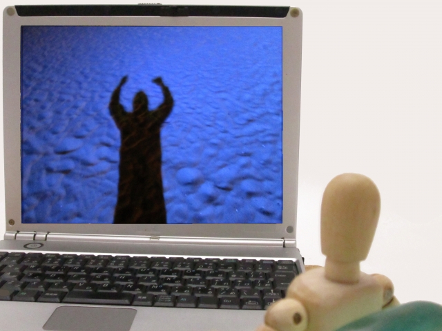 人形がパソコンの画面を見ている画像